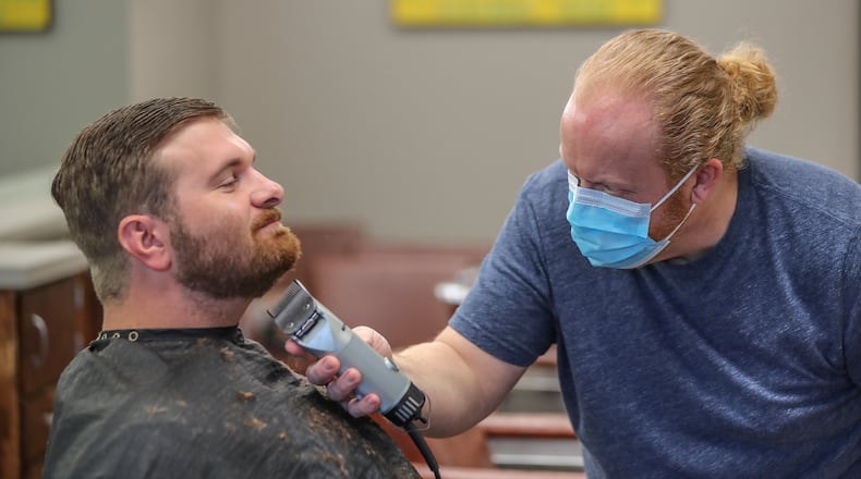 At the Peachtree Battle Barber Shop in Atlanta, barber and owner Chris Edwards wears a mask as he cuts the hair of customer David Boswell on Friday, April 24, 2020. The first phase of Gov. Brian Kemp’s plan to reopen Georgia during the coronavirus pandemic included barber shops, hair salons and gyms, though not all chose to open their doors. JOHN SPINK/JSPINK@AJC.COM