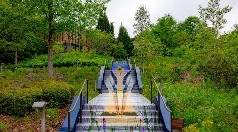 A new staircase mural at the Chattahoochee Nature Center depicts a pair of Great Blue Herons standing in the riverbed among native cattail and pickerelweed. In the background, a vibrant sunset highlights trees along the riverbank. Courtesy Chattahoochee Nature Center