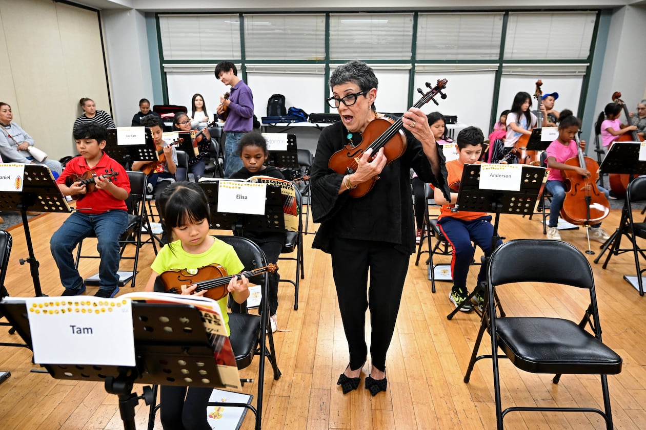 Juana Alzaga (standing) instructs members of the Buford Highway Orchestra Project at the Latin American Association in Brookhaven on Thursday, Nov. 6, 2025. The orchestra, which is comprised mostly of children of parents who lack legal status, will be featured in the documentary “La Orquesta” coming this month to PBS. (Hyosub Shin/AJC)
