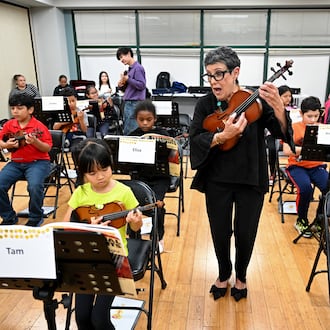 Juana Alzaga (standing) instructs members of the Buford Highway Orchestra Project at the Latin American Association in Brookhaven on Thursday, Nov. 6, 2025. The orchestra, which is comprised mostly of children of parents who lack legal status, will be featured in the documentary “La Orquesta” coming this month to PBS. (Hyosub Shin/AJC)