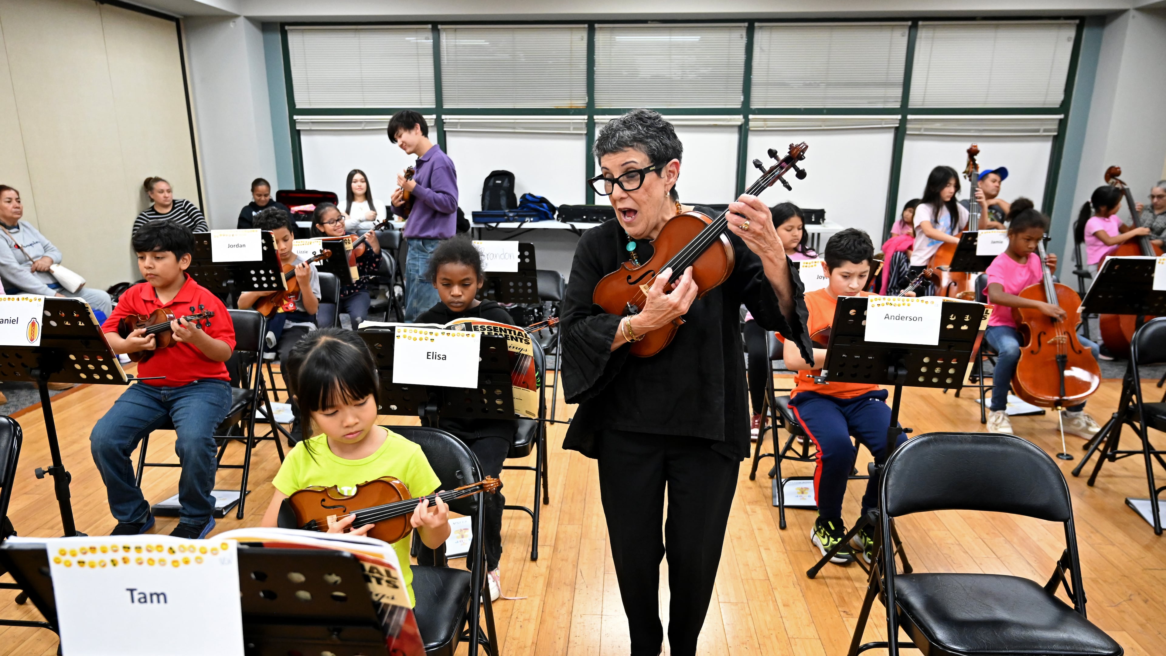 Juana Alzaga (standing) instructs members of the Buford Highway Orchestra Project at the Latin American Association in Brookhaven on Thursday, Nov. 6, 2025. The orchestra, which is comprised mostly of children of parents who lack legal status, will be featured in the documentary “La Orquesta” coming this month to PBS. (Hyosub Shin/AJC)