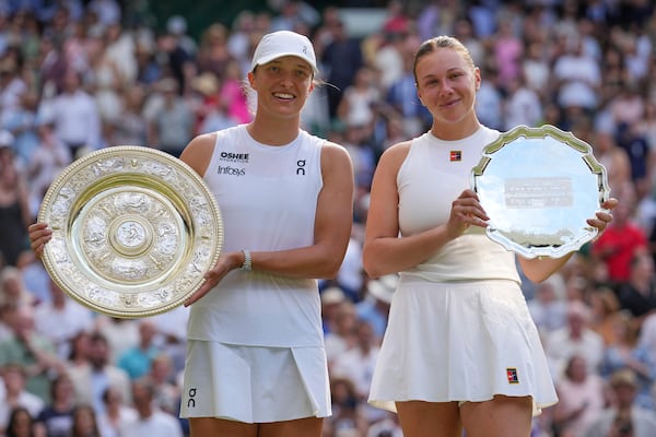 Poland's Iga Swiatek, left, celebrates with the trophy after beating Amanda Anisimova of the U.S., right, to win the women's singles final at the Wimbledon Tennis Championships in London, Saturday, July 12, 2025. (AP Photo/Kin Cheung)