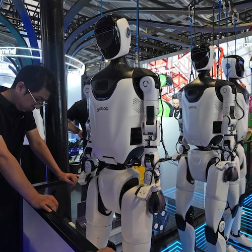 FILE - A worker reacts near a line of humanoid robots displayed at the World AI Conference in Shanghai, Friday, July 17, 2026. (AP Photo/Ng Han Guan, file)