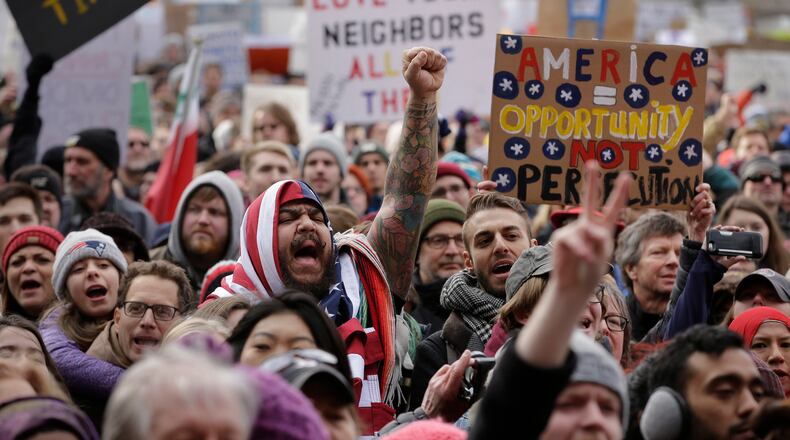 Izzy Berdan, of Boston, center, wears an American flags as he raises his arm and chants slogans with other demonstrators during a rally against President Trump's order that restricts travel to the U.S., Sunday, Jan. 29, 2017, in Boston. On Thursday, Feb. 16, 2017, immigrants across the nation will take part in "A Day Without Immigrants," a protest meant to show how immigrant dollars impact the U.S. economy. (AP Photo/Steven Senne)