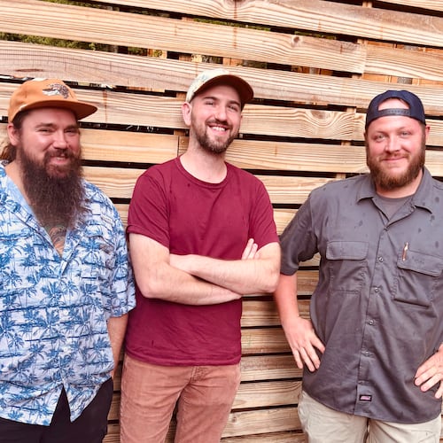 Three smiling men in nice casual clothing standing in front of a wooden-slat fence.