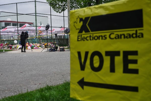 A voting sign stands near a memorial for victims after a vehicle drove into a crowd during a Filipino heritage festival in Vancouver, British Columbia, Monday, April 28, 2025. (AP Photo/Lindsey Wasson)