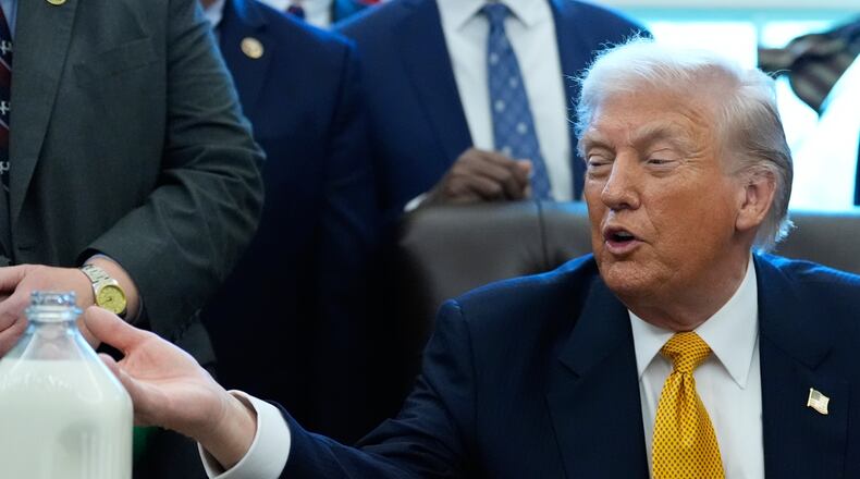 President Donald Trump gestures to a container of milk before he signs a bill that returns whole milk to school cafeterias across the country, in the Oval Office of the White House, Wednesday, Jan. 14, 2026, in Washington. (AP Photo/Alex Brandon)