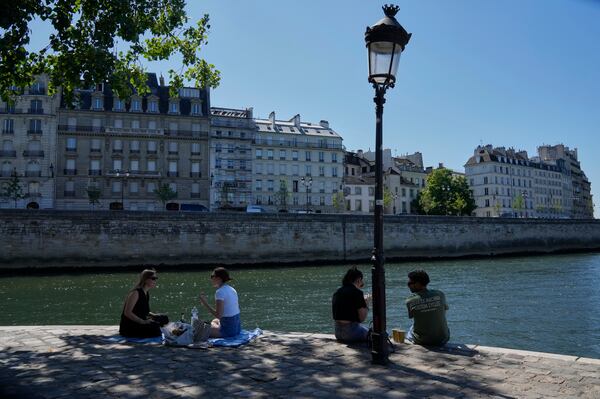 People sit in the shade along the Seine river in Paris, Sunday, June 29, 2025. (AP Photo/Michel Euler)