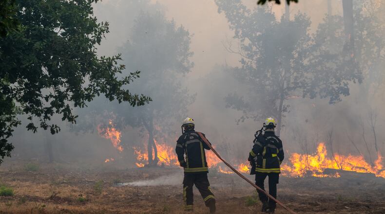 Fiirefighters spray water in a burning forest in the Lège-Cap-Ferret region, western France, Friday, July 24, 2026. (AP Photo/Caroline Blumberg)