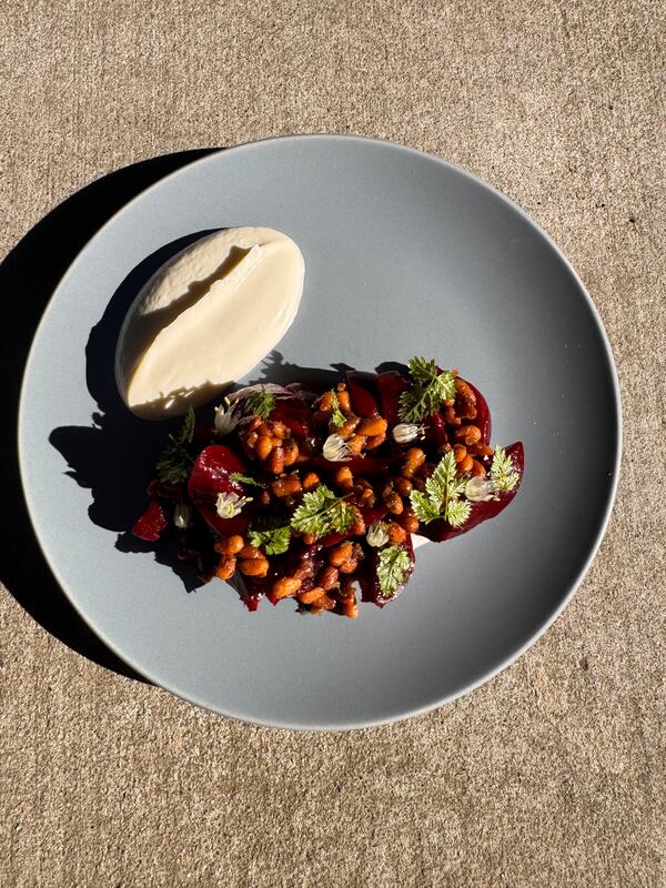 A medley of chopped beats cooked with pine nuts, served with kombu and garnished with whole mint leaves, is arranged on a plate. A large quenelle of smoked yogurt is on the side.