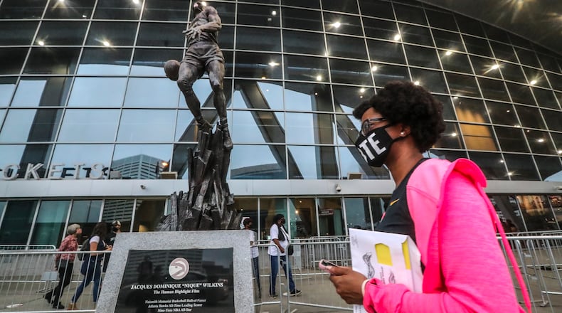 Ashley Nealy makes her way past the statue of Dominique Wilkins as she waited to vote on Monday, Oct. 12, 2020 at State Farm Arena in downtown Atlanta. Eager Georgia voters swarmed to polling places Monday morning, waiting in lines created by high turnout and technical problems at the start of three weeks of early voting before Election Day. (John Spink / John.Spink@ajc.com)