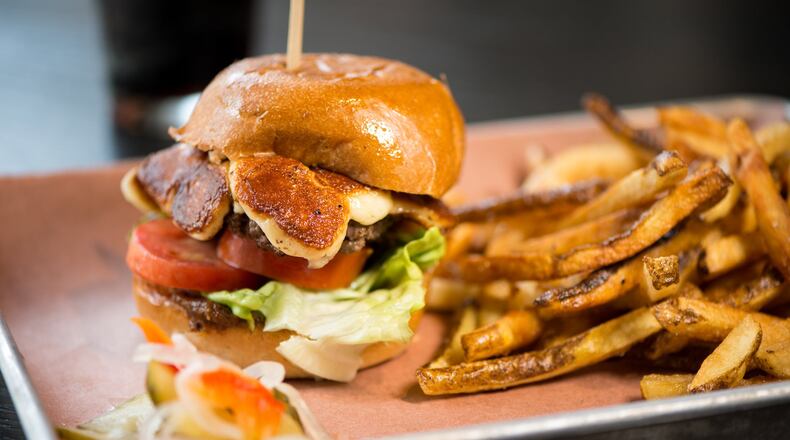 The Big Greasy brisket burger at Loyal Tavern comes topped with white cheddar cheese curds, lettuce, tomatoes, house-made bacon jam and garlic aioli, and is served on a toasted bun. Mia Yakel for The Atlanta Journal-Constitution