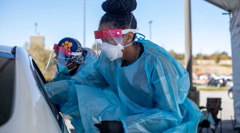11/17/2020 -  Atlanta, Georgia - Two nurses work around a car with four individuals receiving COVID-19 tests at a DeKalb County Department of Health COVID-19 drive-thru testing site in Atlanta, Tuesday, November 17, 2020.  (Alyssa Pointer / Atlanta Journal-Constitution)