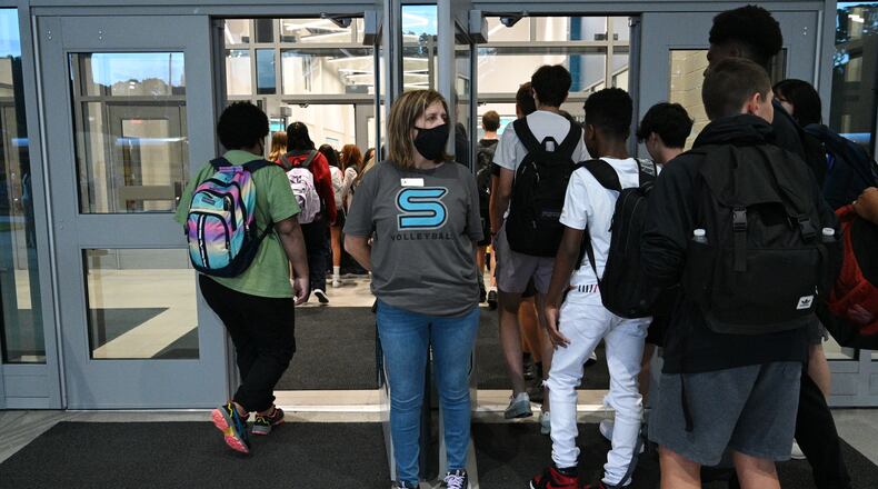 Jejna Mujkic, school staff, greets students arriving for the first day of school at Seckinger High School in Buford on Wednesday, Aug. 3, 2022. All Gwinnett County employees were required to wear masks in school buildings to start the year. The requirement was lifted the second week of classes. (Hyosub Shin / Hyosub.Shin@ajc.com)