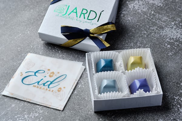 A white box of chocolates is open with four chocolates in metallic colors with a card next to the box that says Eid.
