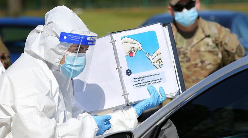 A Walmart pharmacist instructs a motorist how to do a self swab as Georgia Army National Guard Pfc. Joshua Tucker looks on at a mobile COVID-19 drive-through testing site serving rural stretches of Georgia last month. National Guard teams helped staff Georgia's testing strategy. (Curtis Compton/Curtis.Compton@ajc.com)