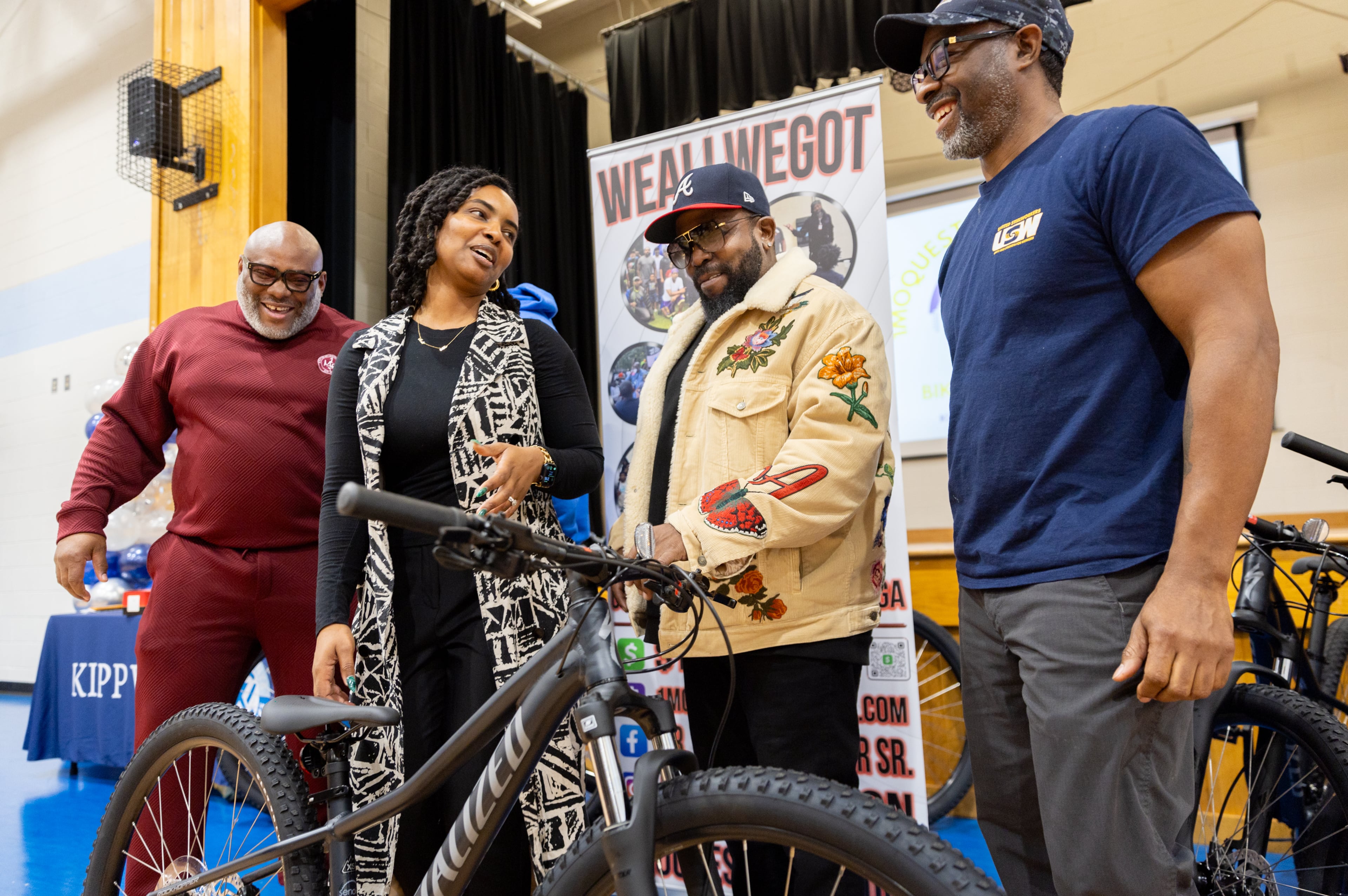 Travis Barber of 1 Mo ?; Jannora Gamble, school social worker; rapper Big Boi; and Lamont Johnson, of 1 Mo ?, laugh during a bike giveaway at Kipp Ways Academy middle school in Atlanta on Monday, December 9, 2024. For the second year in a row Bear Strong partnered with Specialized bikes and Senoia bike shop to award middle school children who have been recognized by their school as most improved, and great attendance. (Arvin Temkar / AJC)