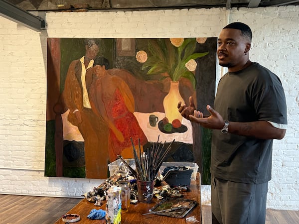 Patrick Eugène gives a tour of his new art studio at the Goat Farm Arts Center on Sept. 26, 2025. The painting in the background is a new work he created as part of a series that explores familial relationships inside Black homes and gatherings. (Danielle Charbonneau/AJC)