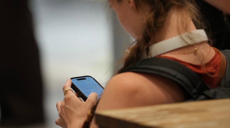 A teenager looks at her mobile phone in London, Monday, June 15, 2026. (AP Photo/Kin Cheung)