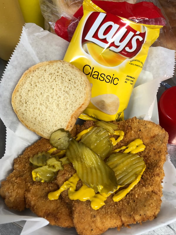 Fried pork tenderloin sandwich topped with mustard and pickles, served with Lay’s potato chips.