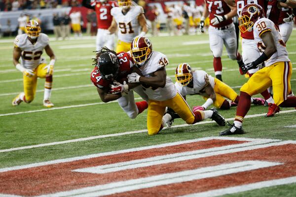 Atlanta Falcons running back Devonta Freeman (24) scores a touchdown as Washington Redskins strong safety Trenton Robinson (34) and Washington Redskins cornerback Bashaud Breeland (26) defend during the second half of an NFL football game, Sunday, Oct. 11, 2015, in Atlanta. (AP Photo/John Bazemore)