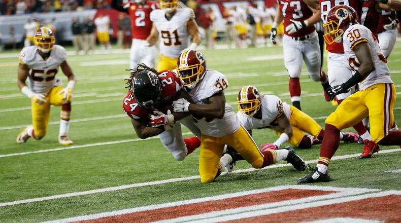 Atlanta Falcons running back Devonta Freeman (24) scores a touchdown as Washington Redskins strong safety Trenton Robinson (34) and Washington Redskins cornerback Bashaud Breeland (26) defend during the second half of an NFL football game, Sunday, Oct. 11, 2015, in Atlanta. (AP Photo/John Bazemore)