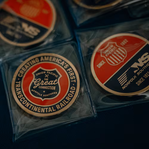 Collector coins labeled “The Great Connection,” referring to the proposed merger between Union Pacific and Norfolk Southern, sit on a table at Railway Age’s Next Generation Freight Rail conference where the two companies were presenting at the Union League Club of Chicago on March 10, 2026 in Chicago. (Jamie Kelter Davis for the AJC)
