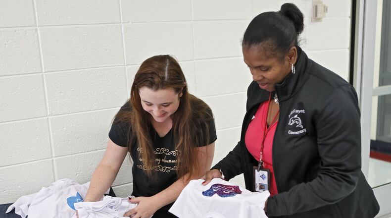 Nikki Rajahn shows North Fayette Elementary School Principal Lisa Moore some of the T-shirt designs from a schoolwide competition encouraging students to submit anti-bullying designs and uplifting slogans. For the first day of school, her son Blake, a subject of bullying, wore a personalized T-shirt that said “I Will Be Your Friend” to reach out to others who might need a friend. BOB ANDRES / ROBERT.ANDRES@AJC.COM