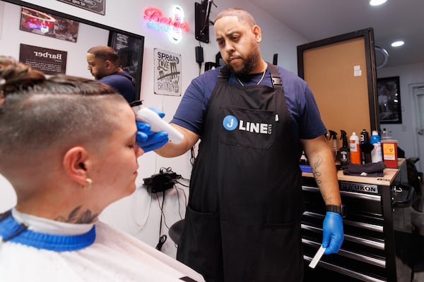 J-Line barbershop owner Jason Zervos (right) cleans up customer Wuski’s edges in Atlanta on Thursday, July 2, 2026. J-Line is located in a suite space made up of three stacked shipping containers. (Estela Muñoz/AJC)