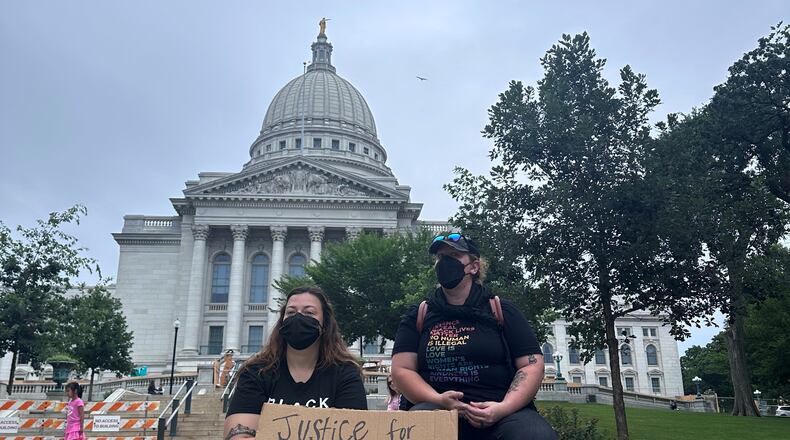 Lilly Nimmer, left, and Reba Bergmann, right, hold a sign to protest the police shooting of Corey Ruiz outside of the Wisconsin state Capitol during the weekly farmers market on Saturday, July 25, 2026, in Madison, Wisconsin. (AP Photo/Scott Bauer)