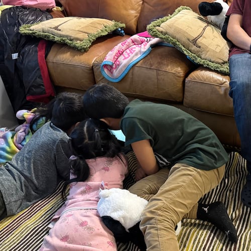 A boy sits on the couch of a Minneapolis safe house Friday, Jan. 16, 2026, as his younger siblings and niece play on the floor beside him after they fled their home because they were sought by federal immigration enforcement agents. (AP Photo/Jack Brook)