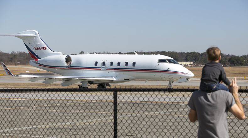 A man and a young boy watch as a private jet moves along the tarmac at DeKalb-Peachtree Airport. (Casey Sykes for The Atlanta Journal-Constitution)