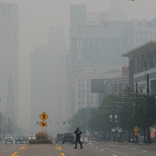 A pedestrian crosses the street as the Detroit city skyline is obscured during poor air quality due to smoke from Canadian wildfires Thursday, July 16, 2026, in Detroit. (AP Photo/Paul Sancya)