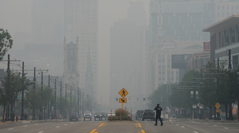 A pedestrian crosses the street as the Detroit city skyline is obscured during poor air quality due to smoke from Canadian wildfires Thursday, July 16, 2026, in Detroit. (AP Photo/Paul Sancya)