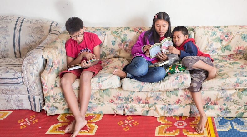 Ram, En Kawli and Bawi reading while seated on the couch in the family living room.  They understand the importance of reading for continued learning of English.