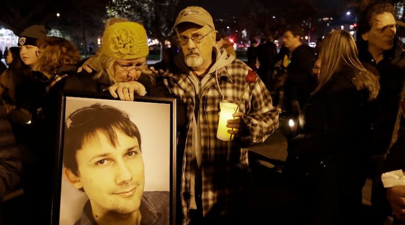 Judy Hough, left, and her husband Brian, center, hold a picture of their son Travis, who died in a warehouse fire, during a vigil at Lake Merritt on Monday, Dec. 5, 2016, in Oakland, Calif. Family members and friends are being notified as firefighters continue a painstaking search for victims of the Oakland warehouse fire. (AP Photo/Marcio Jose Sanchez)