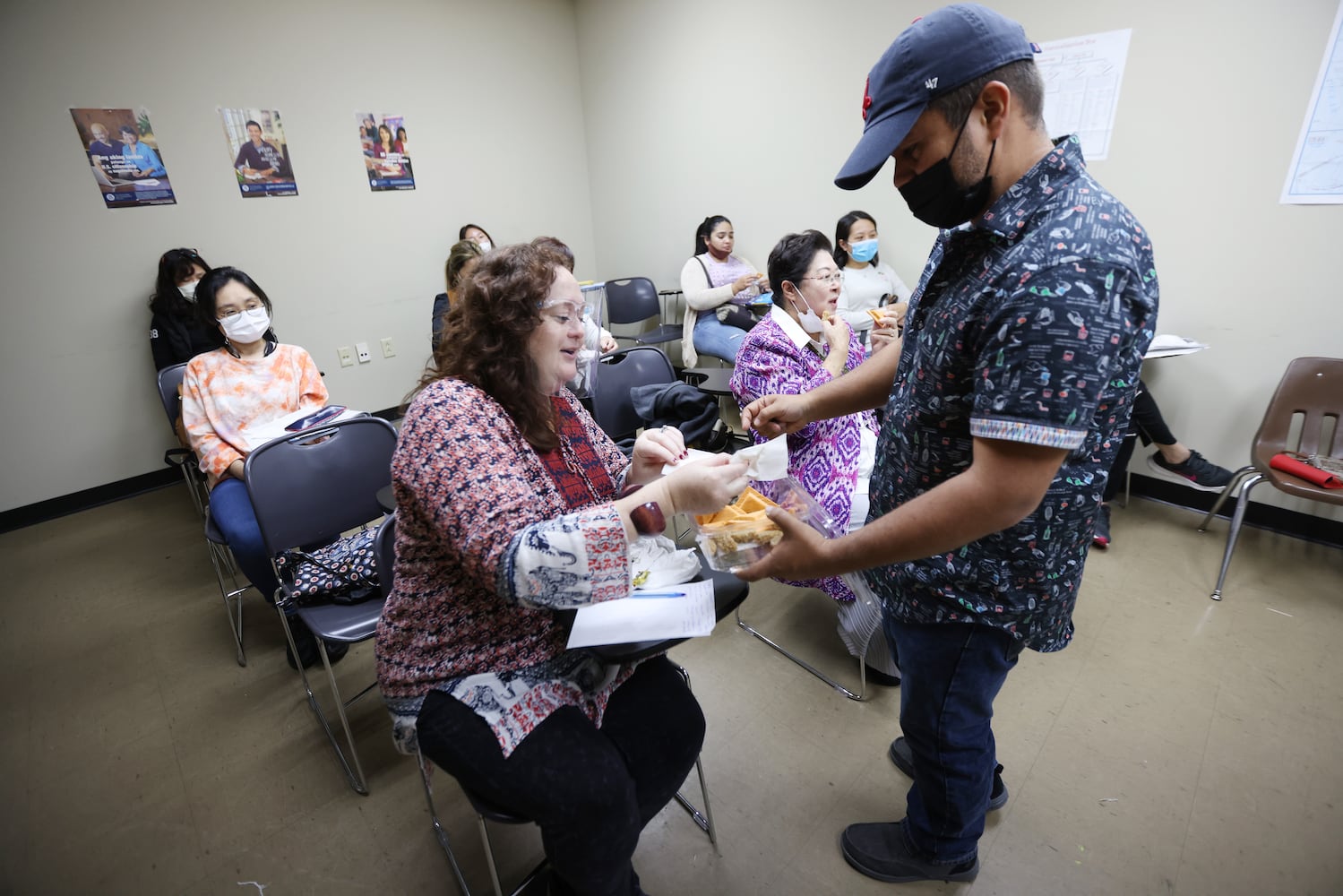 Second level student Alejandro Murillo from Colombia offers teacher Carey Waldrof sweets from his home country during a Center for Pan Asian Community Services class. Murillo gave a presentation to the class about his native country on Nov. 11, 2021. (Miguel Martinez for The Atlanta Journal-Constitution)