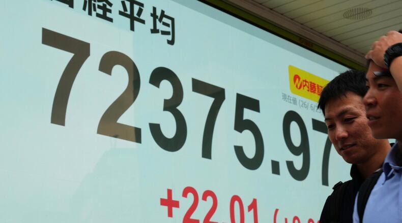 People walk past a monitor showing Japan's Nikkei 225 index at a securities firm in Tokyo, Tuesday, June 23, 2026. (AP Photo/Hiro Komae)