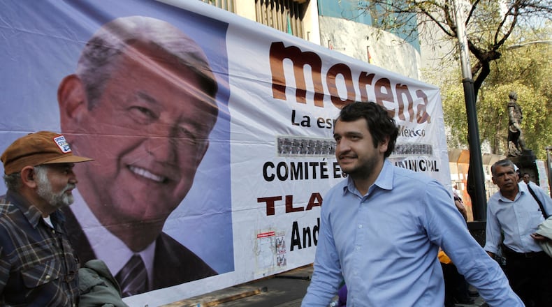 FILE - Andres Lopez Beltran, center, walks past a banner featuring an image of his father, Andres Manuel Lopez Obrador, in Mexico City, Dec. 6, 2013. (AP Photo/Marco Ugarte, File)