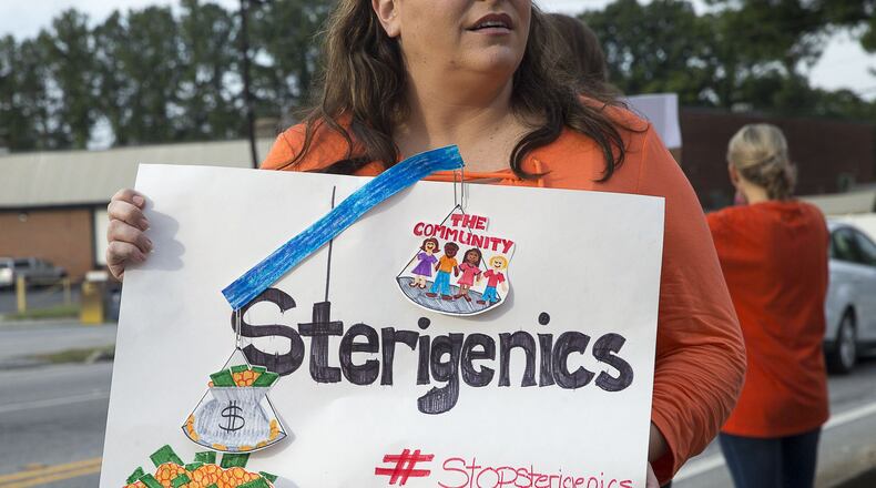 Laura Barnes of Vinings holds a protest sign as she and others gather near the Sterigenics plant in Smyrna, last August. (Alyssa Pointer/alyssa.pointer@ajc.com)