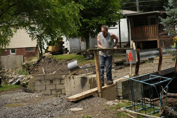 John Black puts up a board over a washed out foot bridge over Battle Run creek, Monday, June 16, 2025, in Valley Grove, W.Va. (AP Photo/Carolyn Kaster)