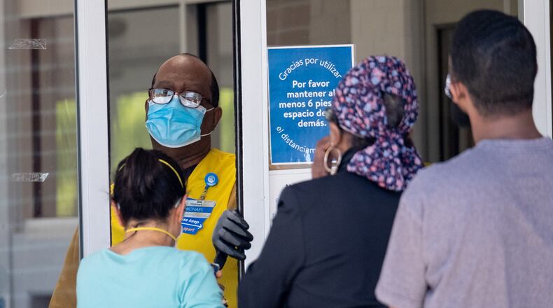A Walmart employee wearing gloves and a mask lets a limited number of customers into a Tucker store Wednesday April 15, 2020. (Ben@BenGray.com for The Atlanta Journal-Constitution)