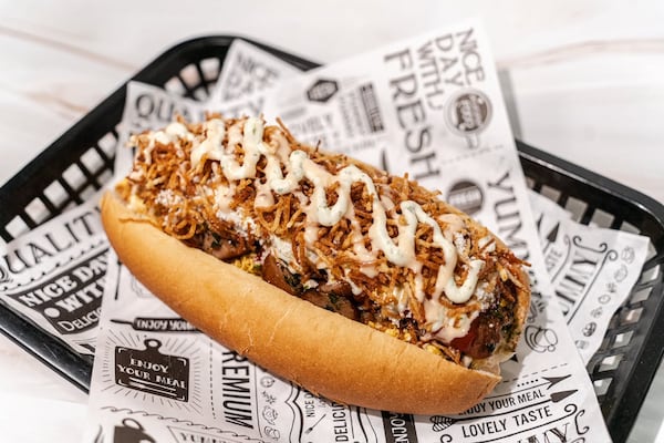 A completely loaded hot dog filled with meat and sauces, resting in a plastic, tissue paper-lined to hot dog basket.