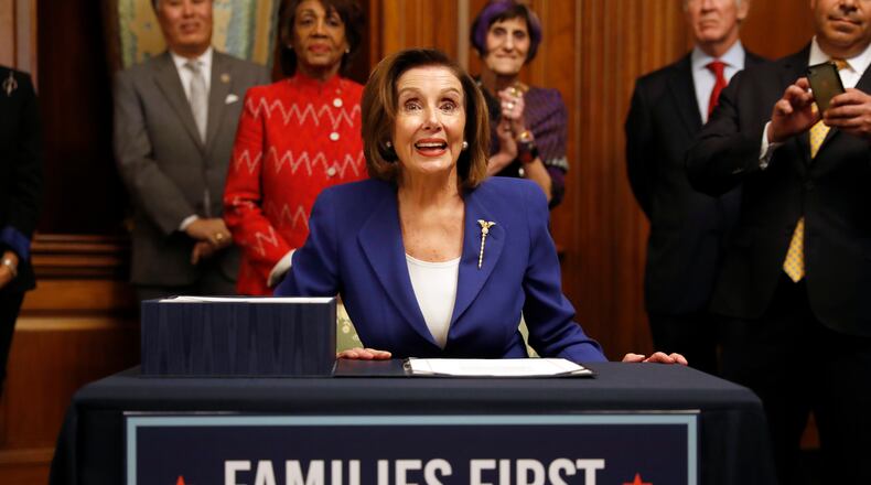 House Speaker Nancy Pelosi of Calif. accompanied by other legislators, signs the Coronavirus Aid, Relief, and Economic Security (CARES) Act. after it passed in the House on Capitol Hill, Friday, March 27, 2020, in Washington. The $2.2 trillion package will head to head to Trump's desk for his signature. (AP Photo/Andrew Harnik)