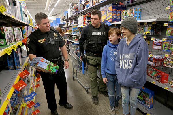 Abel Stevens, 11, center, and his sister Gabriella Bailey, 14, right, of Canton, shop for toys with Sergeant Cody Jones, left, and Deputy Joe Sullivan at Walmart, Tuesday, December 13, 2022, in Canton, Ga. The children were shopping with the Cherokee County Deputies during their annual ‘Shot with a cop’ event to buy toys for underprivileged children. (Jason Getz / Jason.Getz@ajc.com)