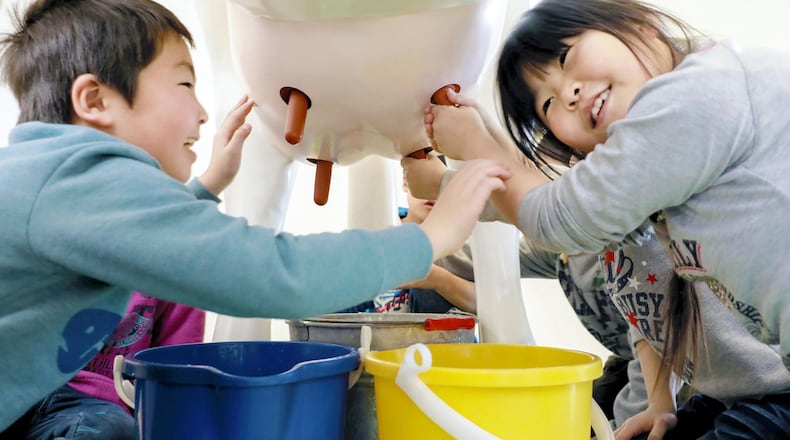 Elementary school students experience milking a cow using a life-size model that squirts out water instead of milk at Meiji Co.'s Moriya Factory, in Moriya, Japan. Photo: Japan News-Yomiuri