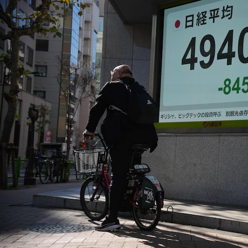 A person on a bicycle waits in front of an electronic stock board showing Japan's Nikkei index at a securities firm Monday, Dec. 1, 2025, in Tokyo. (AP Photo/Eugene Hoshiko)