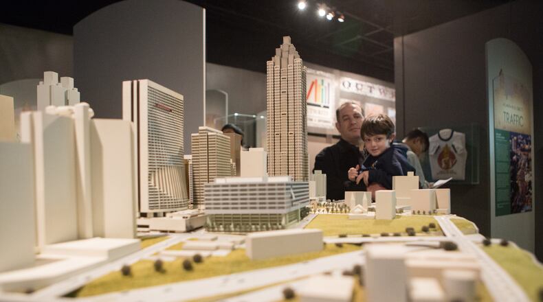 Andrew Tavani, of Buckhead, helps 5 year old Max Tavani get a closer look at the John Portman portion of the 50 Objects exhibit is on display at the Atlanta History Center. On display are 50 city-defining pieces that range from a 1915 Coke bottle mold to Native American artifacts to an 11-foot-long Chick-fil-A billboard cow.