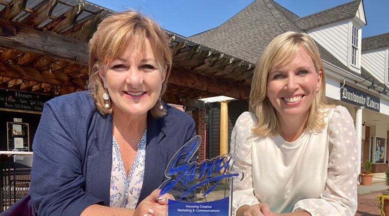 Dunwoody Communications Manager Kathy Florence and Dunwoody Communications Director Jennifer Boettcher pose with the Savvy Award at a painted picnic table in the Dunwoody Village. CONTRIBUTED