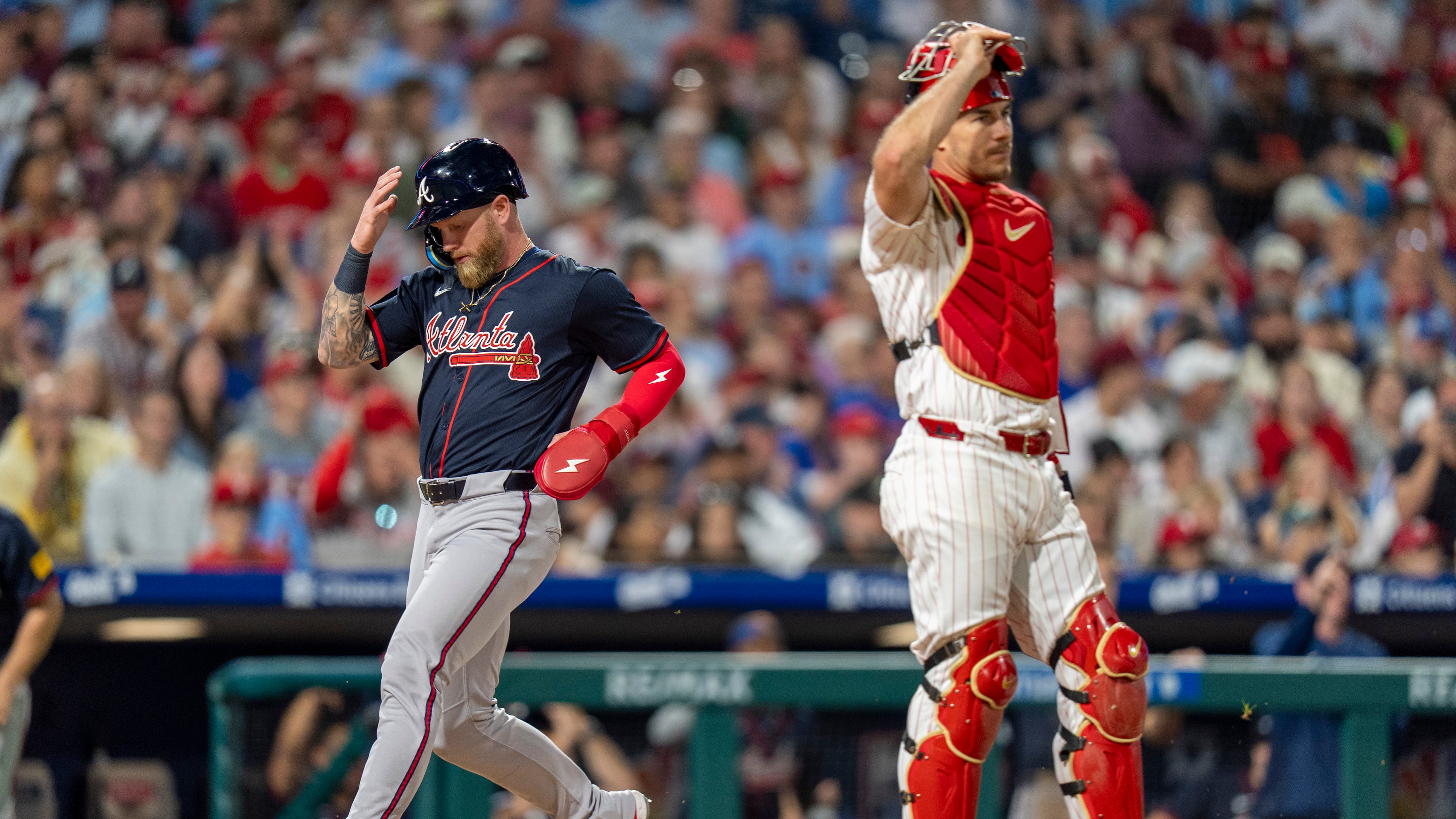 Atlanta Braves' Jake Fraley, left, comes in to score as Philadelphia Phillies catcher J.T. Realmuto, right, looks on during the tenth inning of a baseball game, Saturday, Aug. 30, 2025, in Philadelphia. (AP Photo/Chris Szagola)